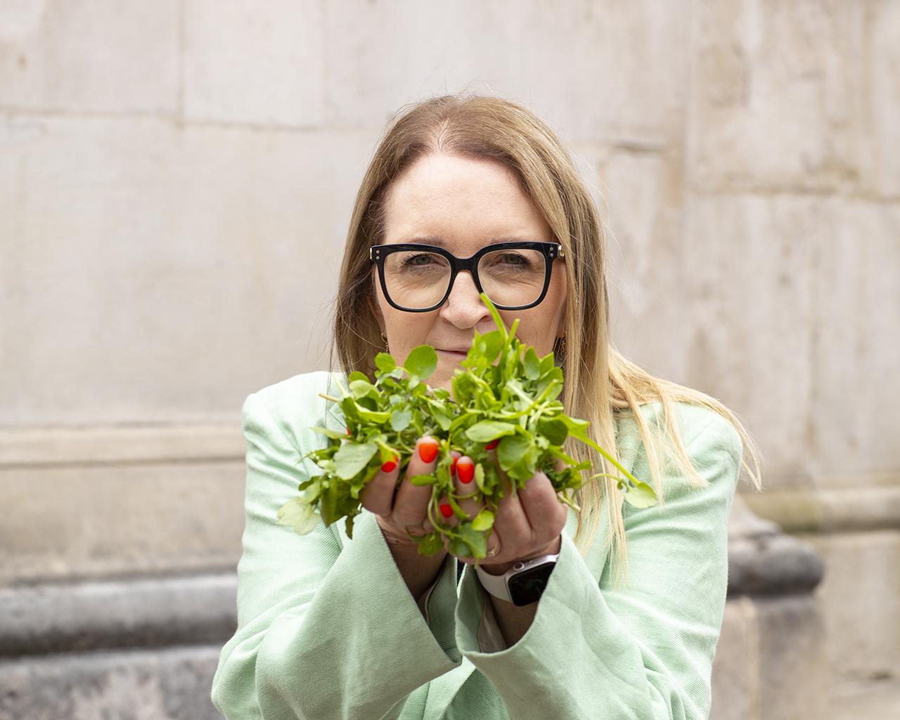 Photo of Prof. Gail Taylor, a blond woman with glasses, holding a handful of leafy greens.